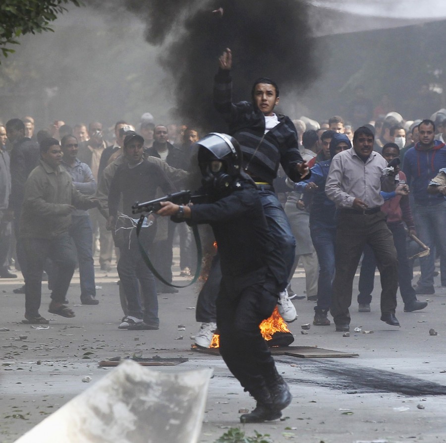 A riot policeman aims a shotgun with rubber bullets at protesters, next to a plainclothes policeman during clashes in a side street near Tahrir Square in Cairo